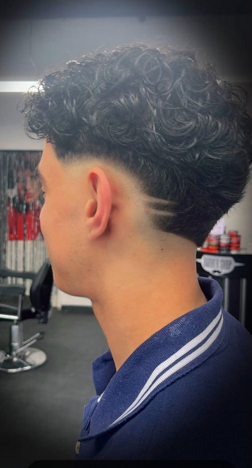 Krullend haar met een strakke taper fade en een geschoren lijn boven het oor
